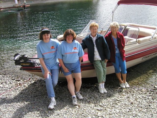 Mary Ann Moog, Lois Evans, Thelma McLain, and Ann LaCroix stroll along the lake and take a rest near a clan boat.